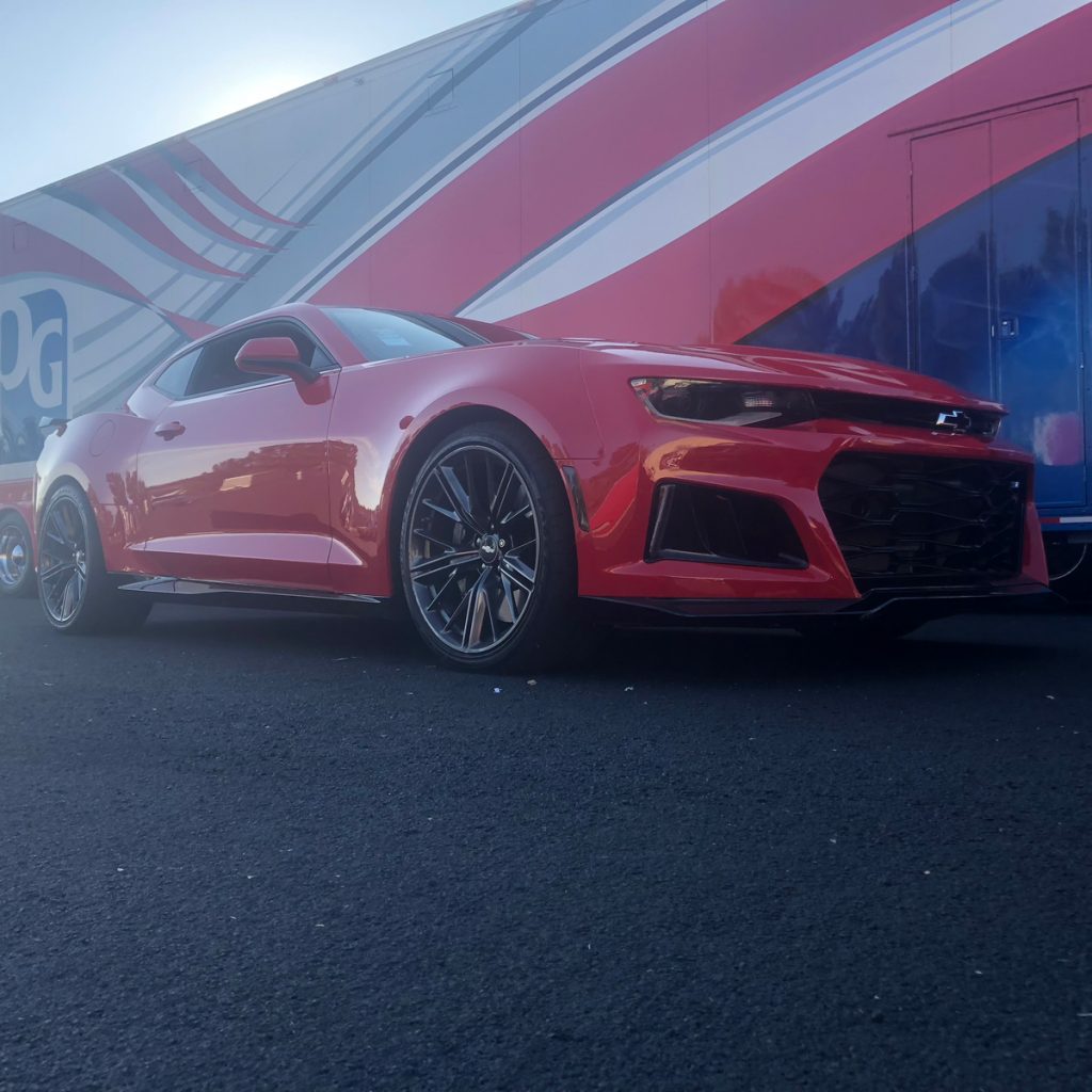 A red Chevy Camaro next to a trailer